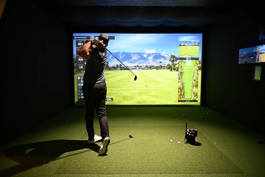 A person playing golf indoors with a large screen displaying a golf course. 3
