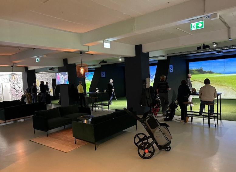 A modern indoor golf simulation area with large screens, seating, and a golf cart. 2
