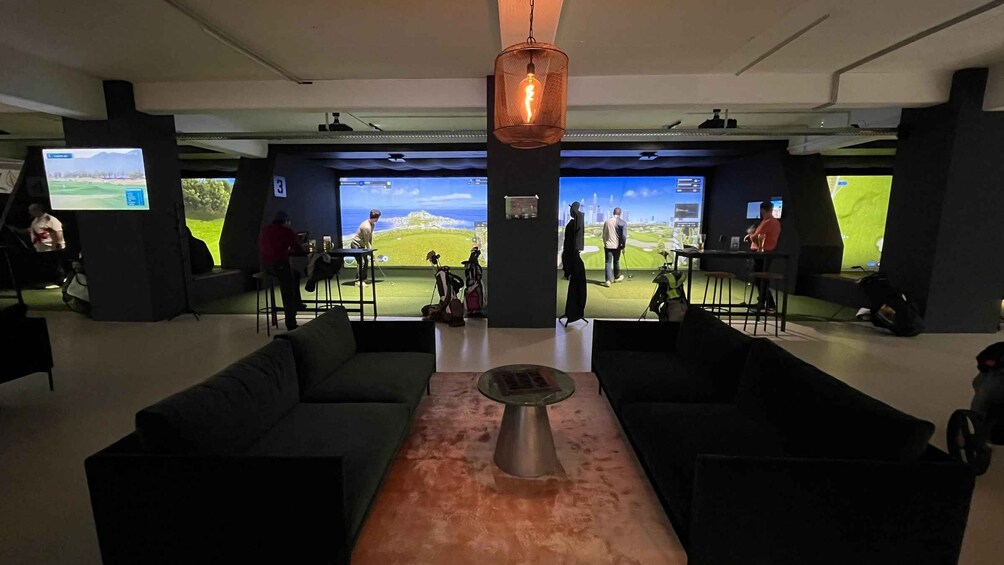 A modern indoor space with a large screen displaying a golf course, a coffee table, and black sofas. 1