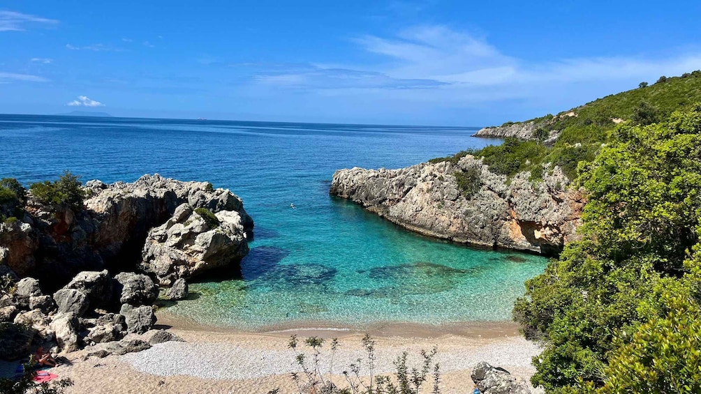 Paesaggio costiero con acque turchesi cristalline, scogliere rocciose e una spiaggia sabbiosa. 1