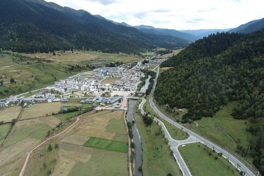 An aerial view of a town with a river, roads, and surrounding green hills. 1