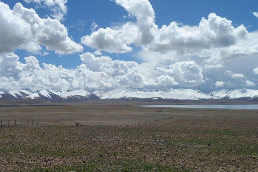 A vast open landscape with a clear sky, distant snow-capped mountains, and a body of water. 2