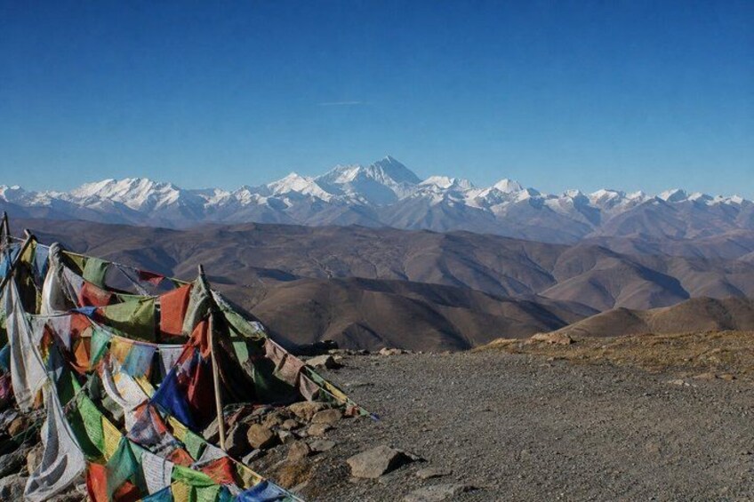 A mountainous landscape with snow-capped peaks, a rocky foreground with colorful prayer flags, and a clear blue sky. 4