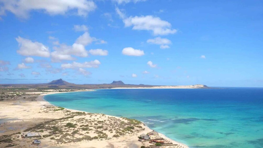 A coastal landscape with clear blue waters, sandy beaches, and distant mountains. 2