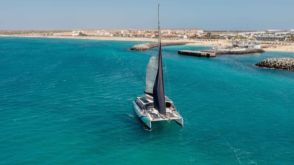 A sailboat on turquoise waters with a coastal town in the background. 1