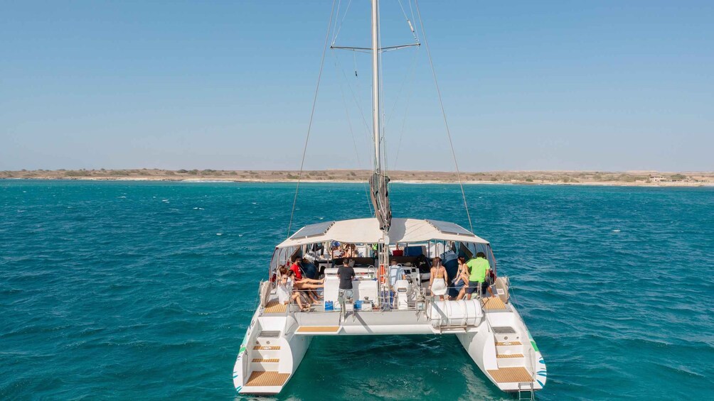 A sailboat with people on board, sailing on a clear blue sea with a sandy beach in the background. 5