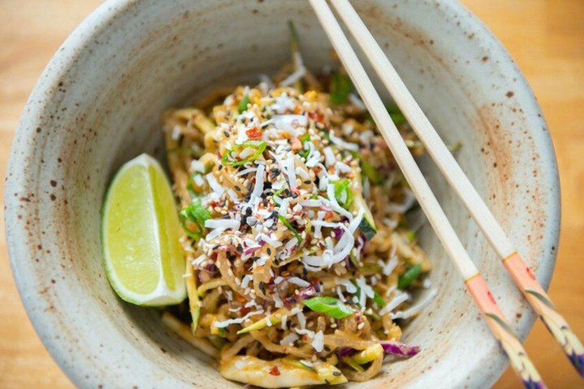 A bowl of noodles garnished with sesame seeds and green onions, with chopsticks and a lime wedge. 2