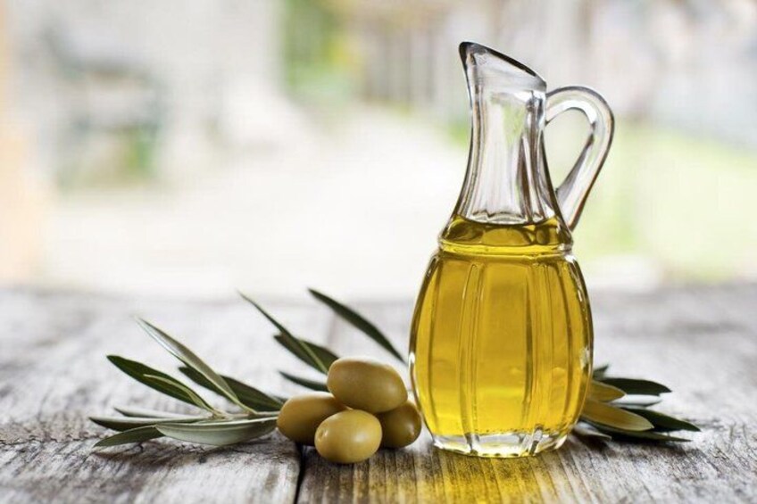 A glass pitcher of olive oil, olives, and olive branches on a wooden surface. 5