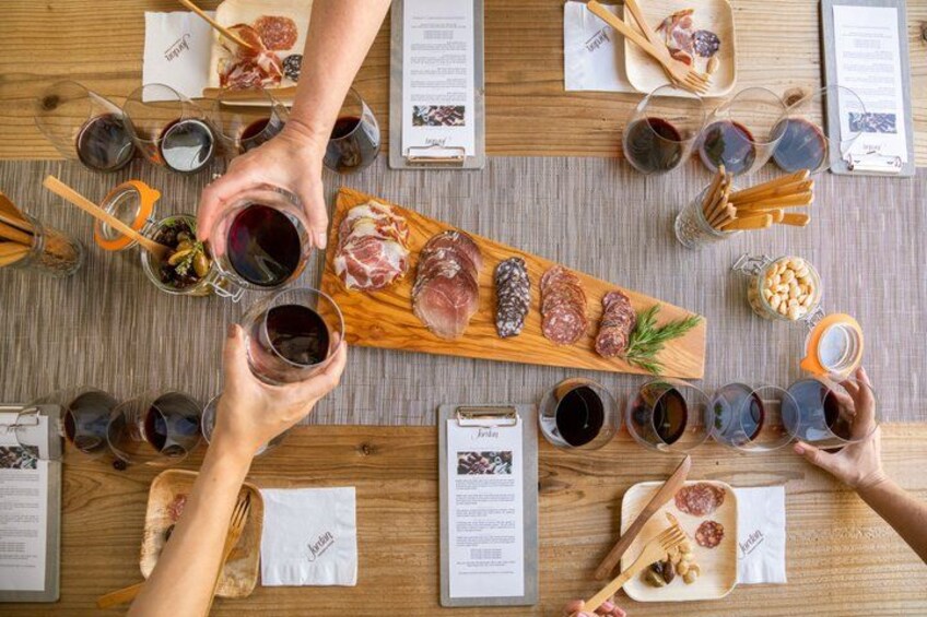 A wooden table with various food items, glasses of red wine, and people holding glasses. 3