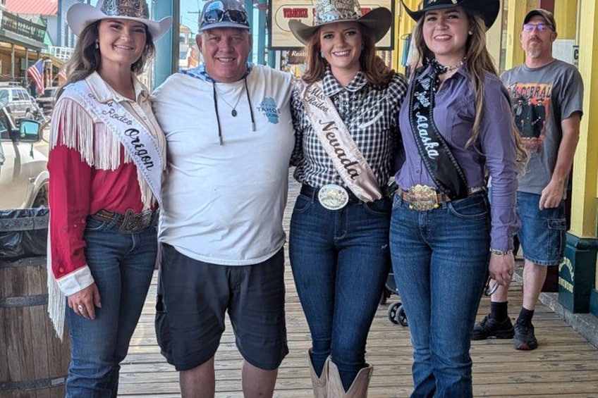 A group of people standing on a wooden deck, some wearing sashes indicating they are beauty pageant winners. 2