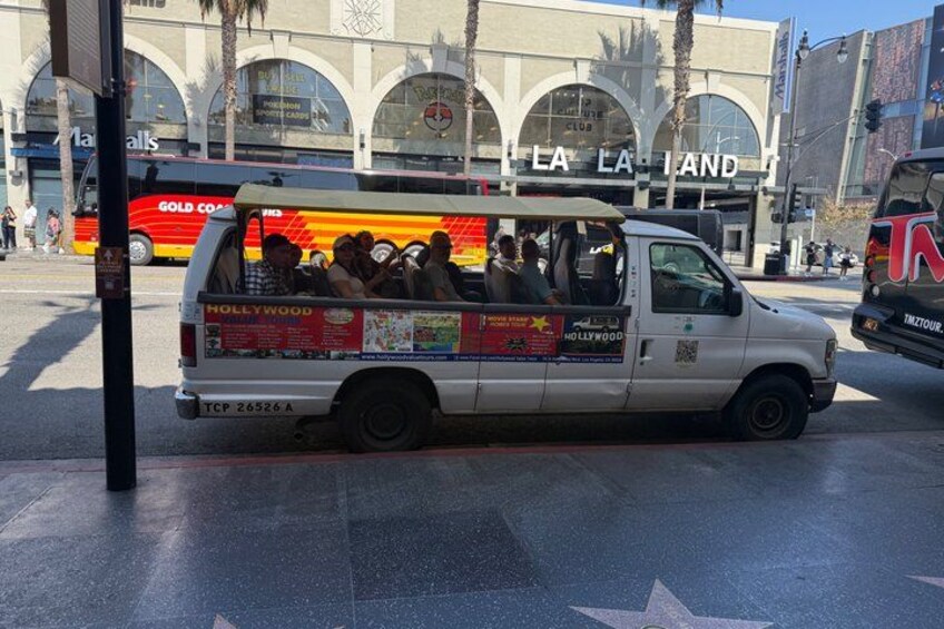 A white van with 'Hollywood' and 'GOLD COAST' on the side parked on a street with a star on the ground. 1