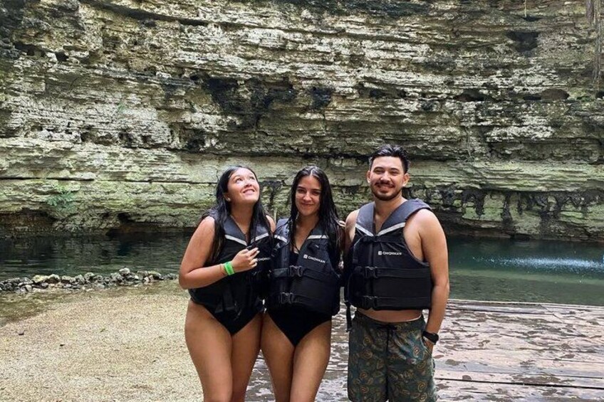 Tres personas con chalecos salvavidas frente a un acantilado rocoso junto a un cuerpo de agua. 2