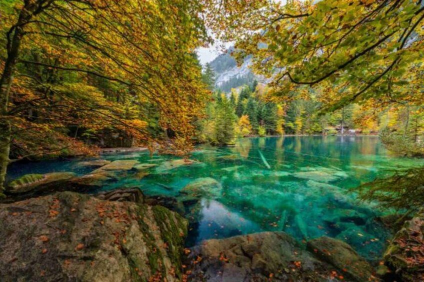 A clear lake surrounded by autumn-colored trees and rocky terrain. 1