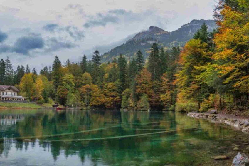 A lake surrounded by autumn-colored trees, a house on the left, and mountains in the background. 5