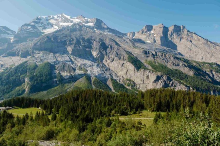 A mountain range with snow-capped peaks, dense forest, and a clear sky. 2