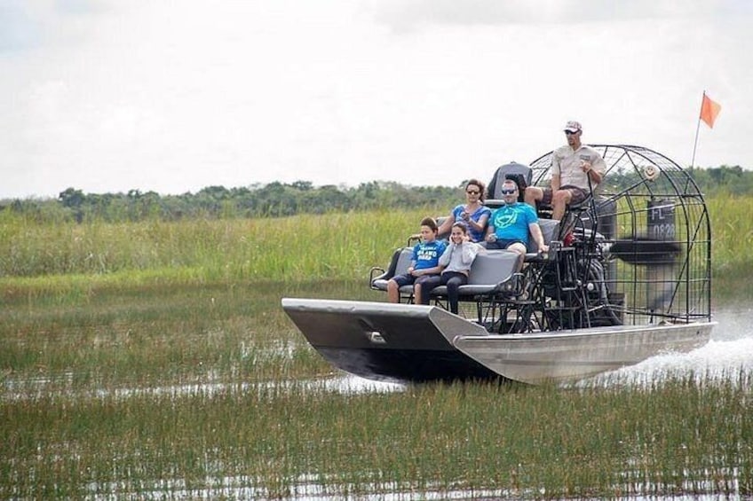 A boat with a canopy and people on it, moving through a marshy area. 5