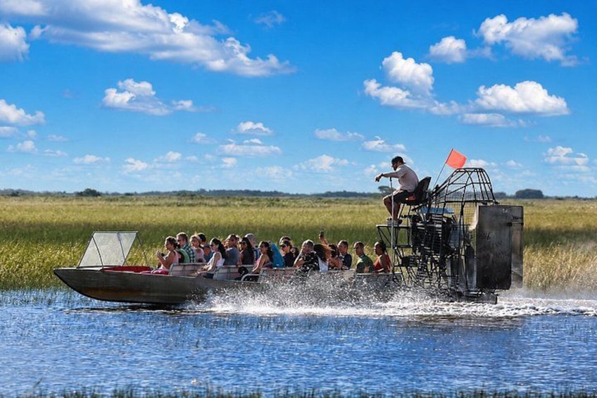 A group of people on a boat with a cage-like structure on top, moving through a body of water with a grassy landscape in the background. 2