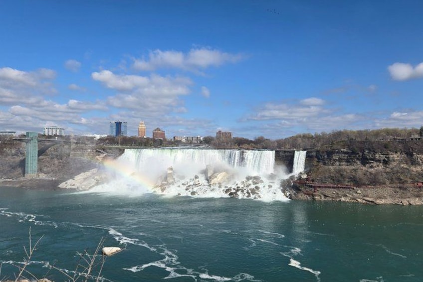 A waterfall with a rainbow, a city skyline in the background, and a bridge. 5