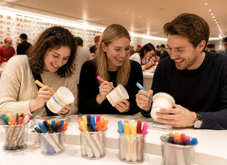 Three people sitting at a table with cups and colorful markers. 2