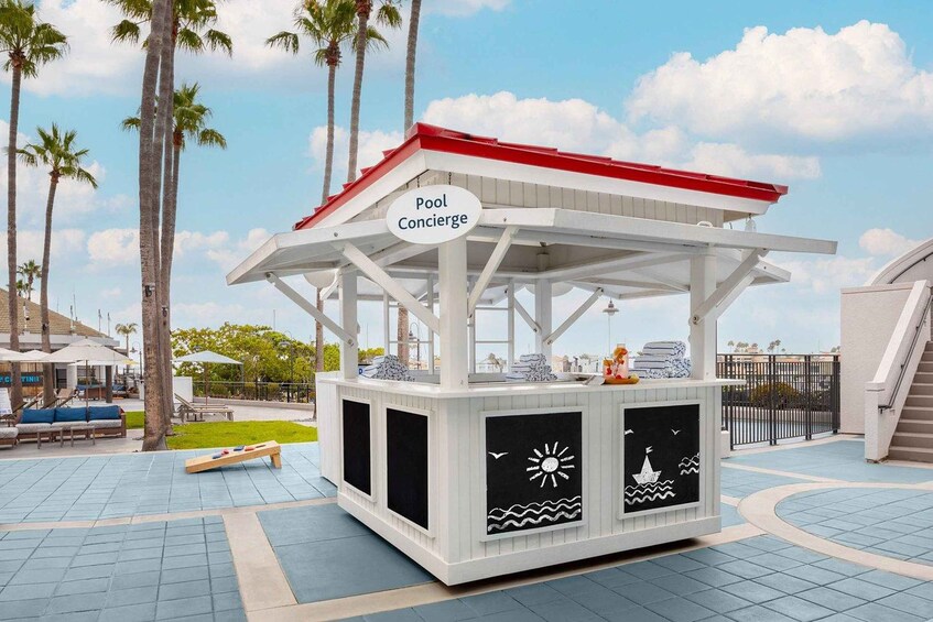 A pool concierge kiosk with a red roof, surrounded by palm trees and a tiled walkway. 2