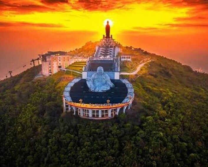 A large statue on a hill with a building in the background. 1