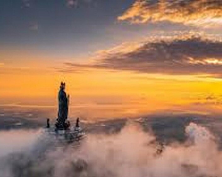 A statue on a platform surrounded by clouds at sunset. 2