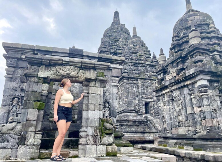 A person standing in front of an ancient stone temple with intricate carvings and multiple domed structures. 5