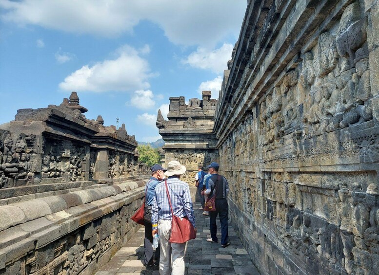 A group of people walking along a stone pathway between ancient stone structures with intricate carvings. 4