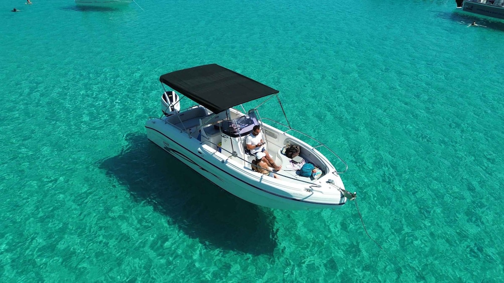 A small motorboat with a canopy, two people, and a child on board, floating on clear turquoise water. 1