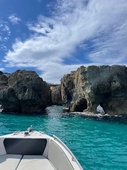 A boat in turquoise waters with rocky cliffs and a clear sky. 2