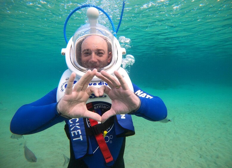 A person underwater wearing a diving helmet and making a heart shape with their hands. 5