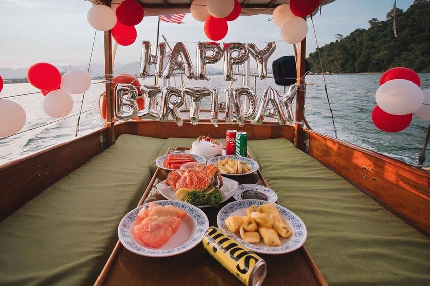 A boat deck with a 'Happy Birthday' balloon decoration, a tray with food, and a scenic water background. 2