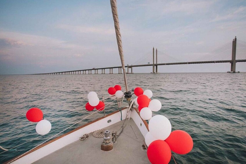 A boat with red and white balloons on the deck, sailing on water with a bridge in the background. 5