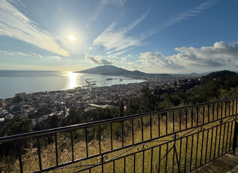 A coastal cityscape with a mountain in the background, a clear sky, and a sun setting or rising over the sea. 3