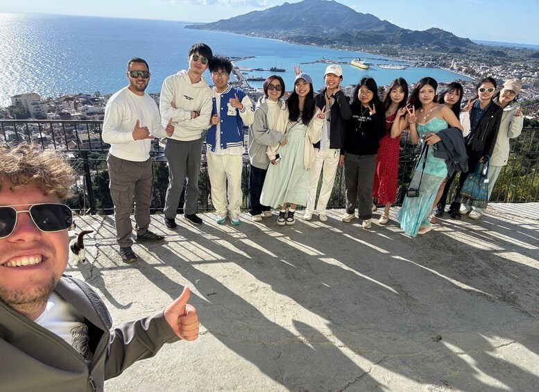 A group of people posing on a concrete ledge with a scenic view of a coastal town and a body of water in the background. 4