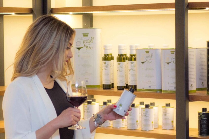 En person holder et vinglas og en produktflaske, mens hylder i baggrunden viser flere lignende flasker. 3