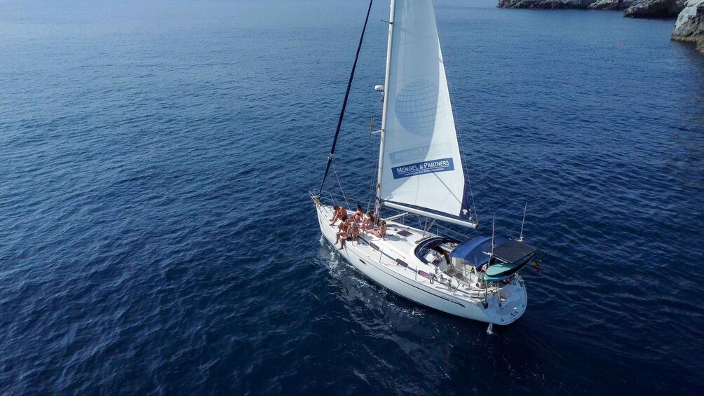 A sailboat with a white sail and a blue logo on the sail, sailing on a calm sea. 1