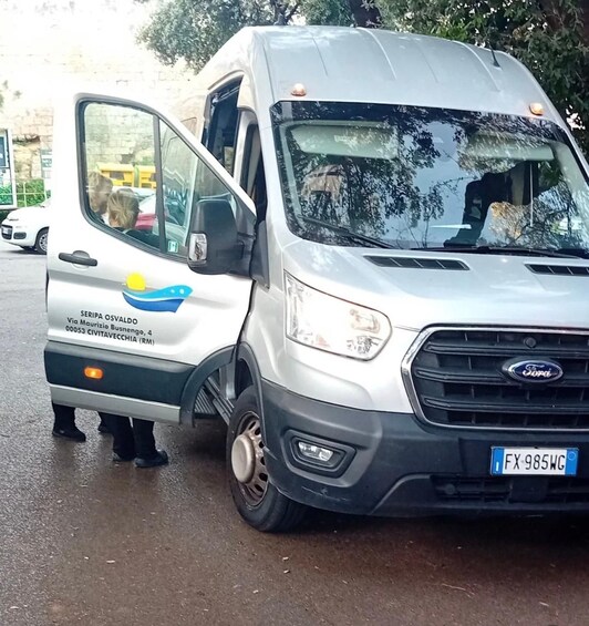 A white van with a blue and yellow logo, parked on a wet road with trees in the background. 3