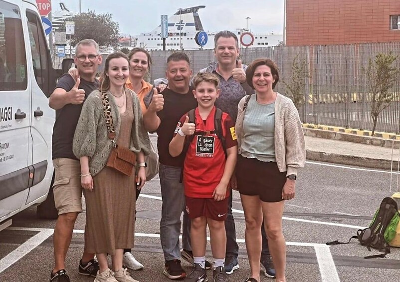 A group of people posing in front of a white van with a ship in the background. 2