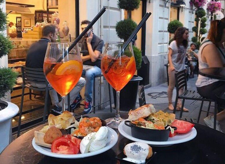 A table with food and drinks, including a plate with bread, tomatoes, and cheese, and two glasses of orange-colored beverage. 4