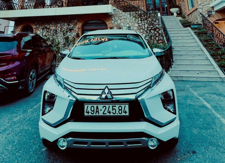 Une voiture blanche de marque Mitsubishi est garée dans une rue, avec un mur de pierre et un escalier en arrière-plan. 5