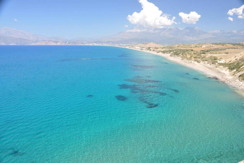 A coastal landscape with clear turquoise waters, sandy beaches, and distant mountains. 1