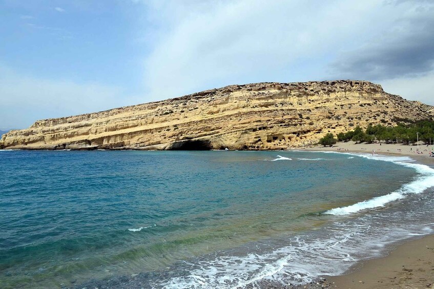 A coastal landscape with a sandy beach, clear blue sea, and a rocky cliff. 2
