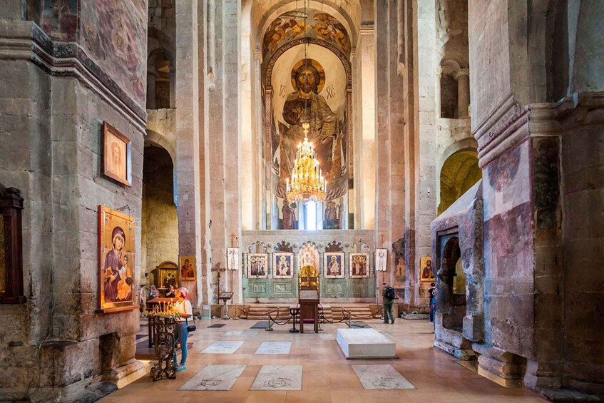 Ein Innenraum einer historischen Kirche mit einem großen Bogen, einer Kandelaber und religiösen Ikonen an den Wänden. 4