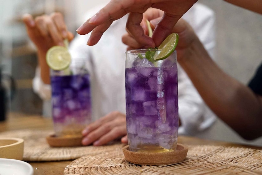 Two glasses of purple beverage with ice cubes and lime slices on coasters. 3