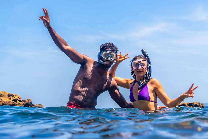 Dos personas haciendo snorkel en aguas azules y cristalinas, con formaciones rocosas al fondo. 4