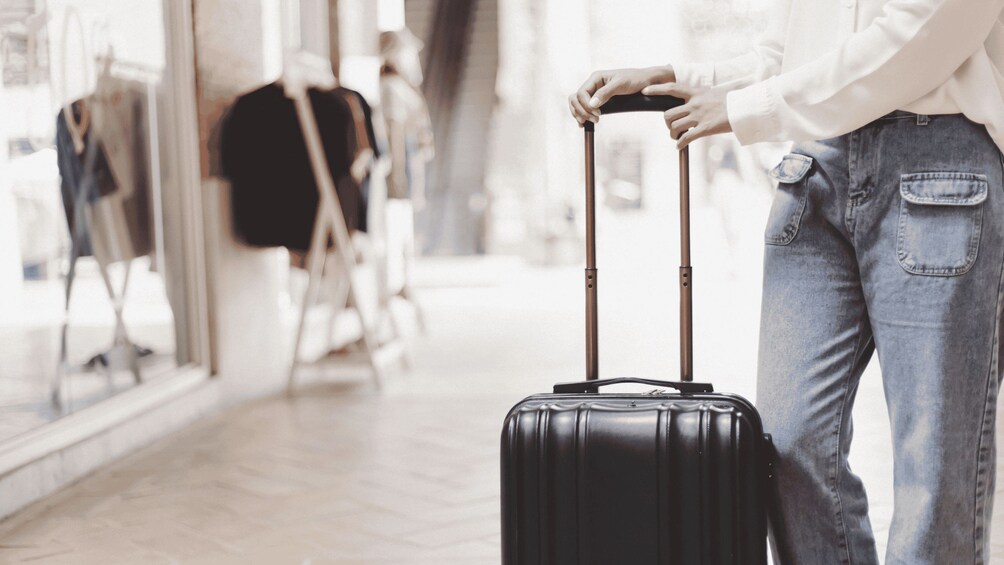 A person with a black suitcase, wearing a white shirt and blue jeans, standing in a shopping area. 4