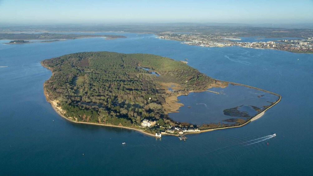 An aerial view of a large island with dense forests, a small settlement, and a clear blue sea. 1