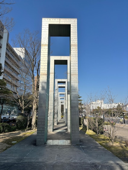 Une structure architecturale moderne, dotée d’un espace central ouvert et entourée de piliers, située dans un parc urbain avec des arbres et un ciel dégagé. 4
