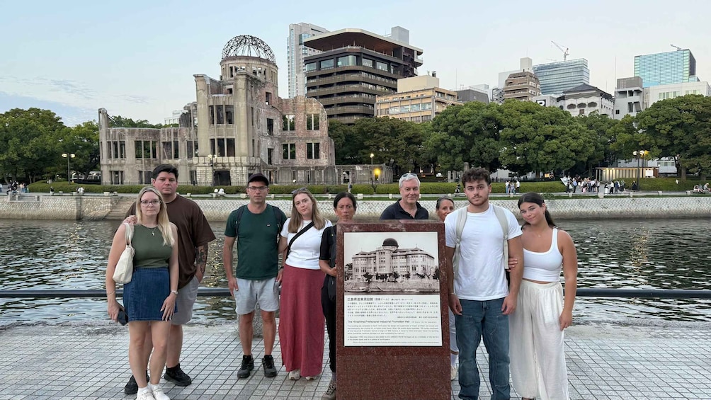 Un groupe de personnes se tient au bord de l’eau, avec un bâtiment historique et des gratte-ciel modernes en arrière-plan. 2
